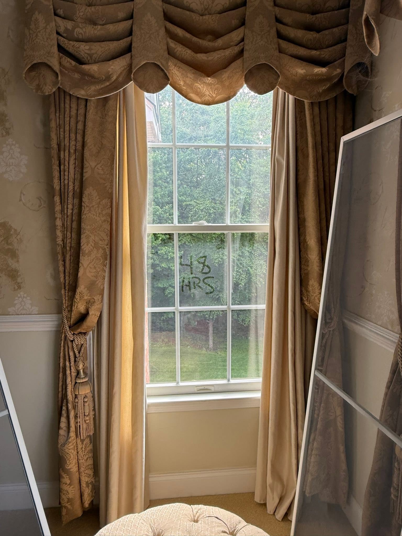 Tall window with draperies before cleaning, hazy glass with 48 HRS written on it