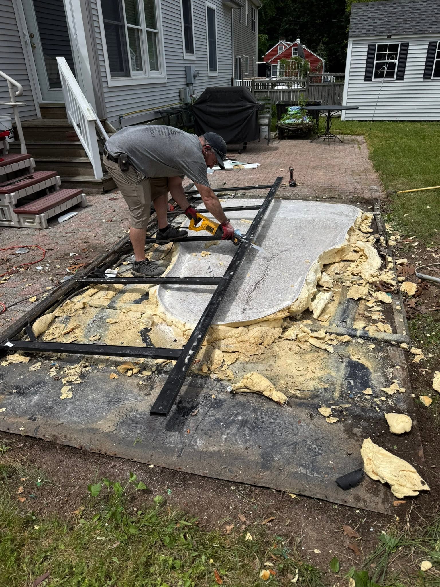 The owner cutting apart a hot tub frame with a reciprocating saw in a backyard